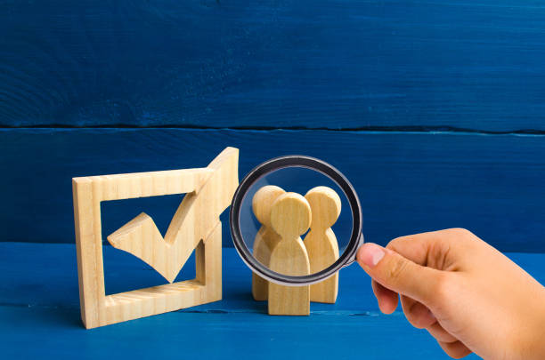 istock The concept of elections and social technologies. constituency electorates. Selective focus Magnifying glass is looking at the Three wooden human figures stand together next to a tick in the box. 1056404612