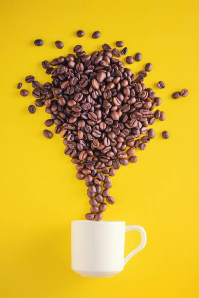 istock Creative food photo. Coffee beans exploding with fireworks from a cup on a yellow background 1056429776