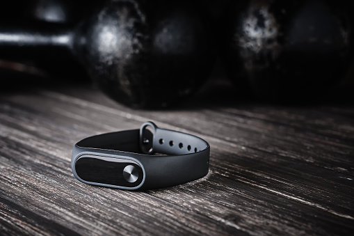 Closeup fitness tracker and old dumbbells on dark wooden background