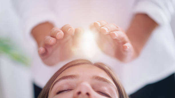 Close Up Of A Relaxed Young Woman Having Reiki Healing Treatment Close up image of relaxed young woman lying with her eyes closed and having Reiki healing treatment in spa center. Energy healing concept. reiki photos stock pictures, royalty-free photos & images