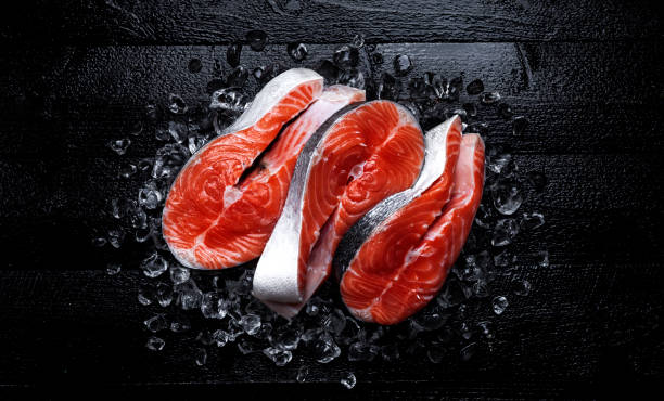 istock Fresh salmon steaks on black wooden background. Top view 1056444602