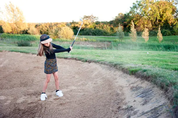 A shot of a young girl hitting the ball out of the bunker during a round of golf.