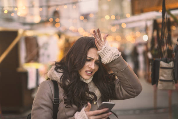 caucásica joven con teléfono inteligente y sostener su cabeza mientras está parado en la calle. - coat concepts danger anger fotografías e imágenes de stock