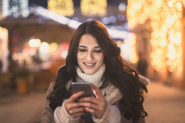 istock Smiling woman using smart phone while standing on the street at night. 1056470002