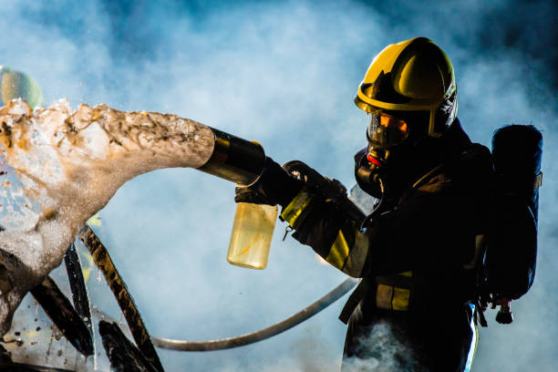 Fireman extinguishing a burning car with foam Close-up photo of a firefighter in full gear extinguishing a fire with foam. extinguishing stock pictures, royalty-free photos & images