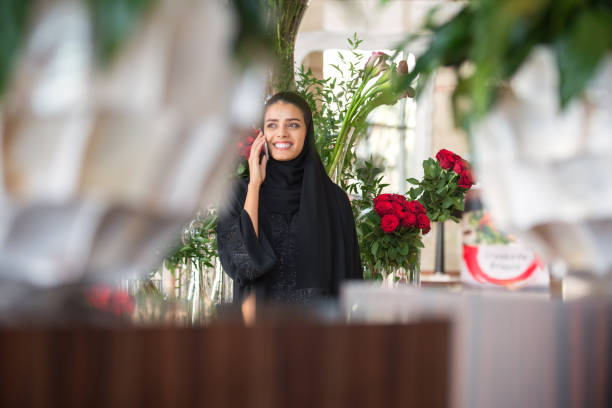 Middle Eastern Florist Talking on Cellphone, Surrounded by Flowers, Vases stock photo