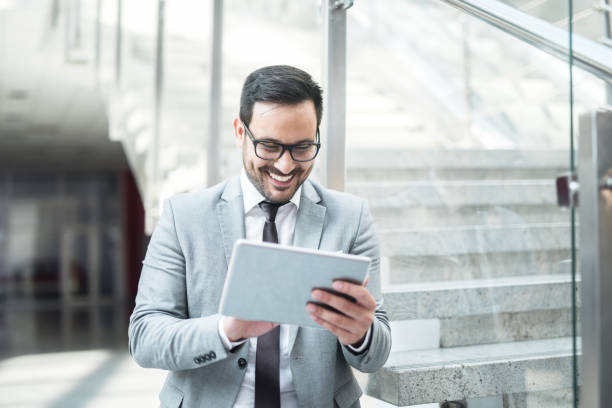 istock Happy young Caucasian businessman using tablet for checking mail while standing in the hall. 1056472800