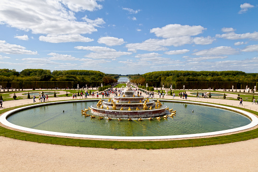 Versailles, France - August 20 2017: Located on the east-west axis just west and below the Parterre d'Eau, is the Bassin de Latone. It is the first fountain you see in the gardens of Versailles in France. Pictured here facing the garden, you can see crowds of tourists gathering around the fountain.
