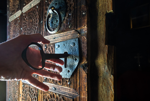Hand unlocking rustic door of wooden church with a big key