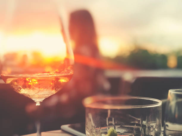 Wine and cocktails on a table at a bar. There is white wine with a fruit cocktail. Backlit at sunset with lens flare