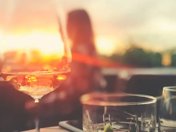 Wine and cocktails on a table at a bar. There is white wine with a fruit cocktail. Backlit at sunset with lens flare