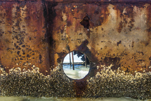 An old ship wreck washed ashore close up looking into a port hole with turquoise water crashing against the inside the boat with orange copper rusted metal tones