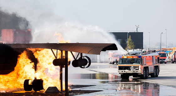 Frankfurt, Germany - October 18, 2018: Airport crash tender SIMBA and plane dummy in flames during a fire drill at FTC (Feuerwehr Training Center). The SIMBA is a large airport fire truck from the Austrian manufacturer Rosenbauer International AG. The FTC (Feuerwehr Training Center) is located at Runway Northwest, nearby fire station 4. Frankfurt International Airport is the largest airport in Germany.