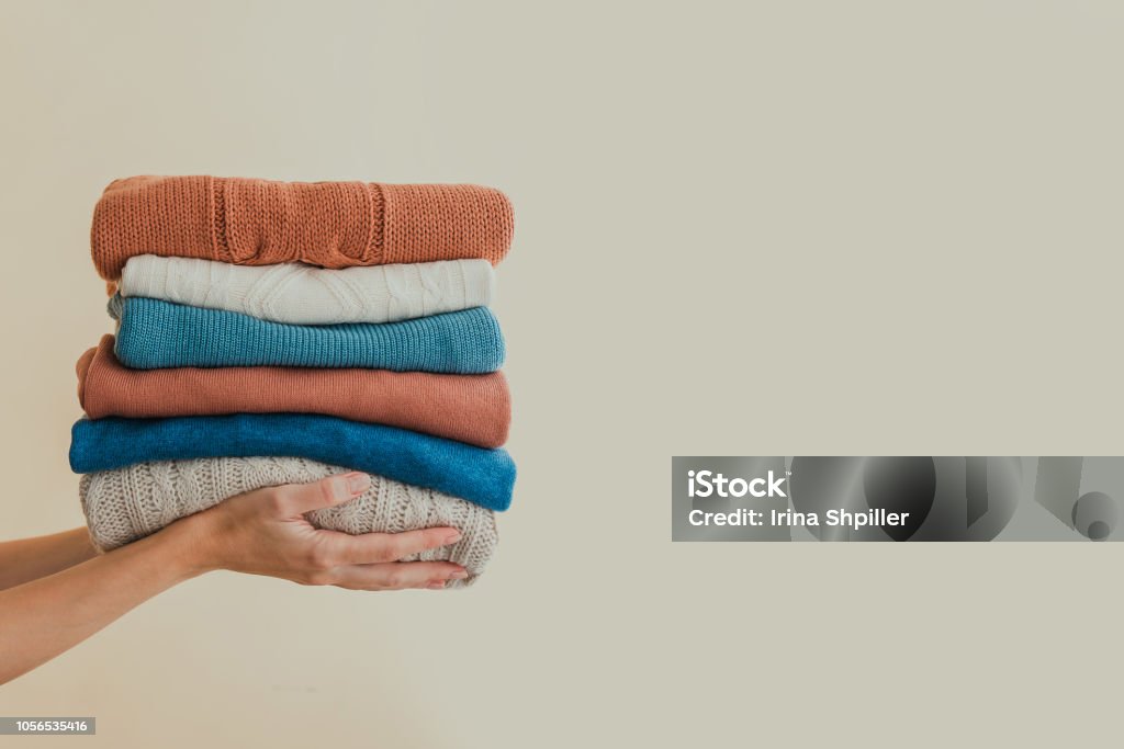 Stack of warm orange and blue pastel weaters, holding in hands Stack of warm orange and blue pastel sweaters, holding in hands. Copy space. Clothing Stock Photo