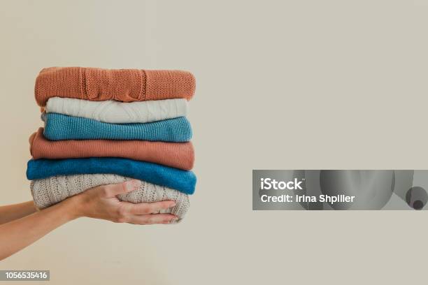 Stack Of Warm Orange And Blue Pastel Weaters Holding In Hands Stock Photo - Download Image Now