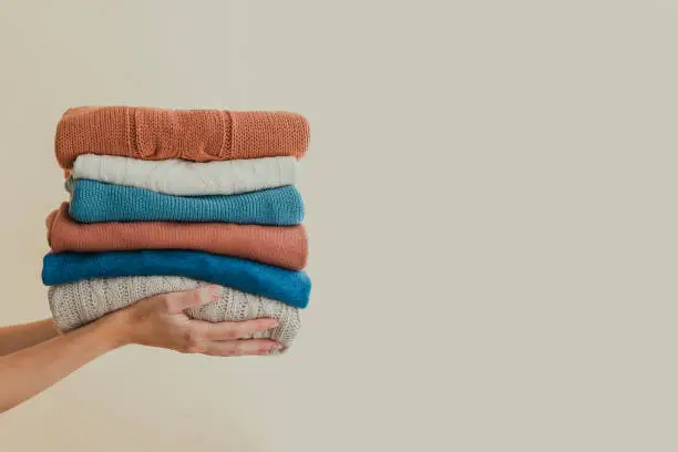 Stack of warm orange and blue pastel sweaters, holding in hands. Copy space.