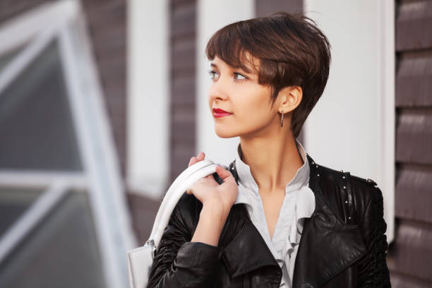 Happy young fashion woman in leather jacket with handbag walking in city street stock photo