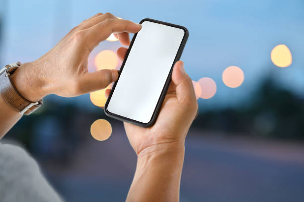 istock Male hand holding blank screen mobile smart phone at street night. 1056564210