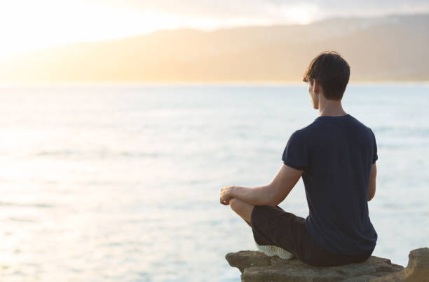 istock Young man meditating on top ocean cliff during sunset. 1056589586