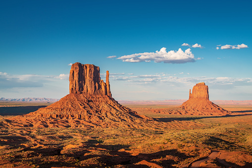 Scenic view to the famous West and East Mittens Buttes in warm late afternoon light under beautiful summer sky. Monument Valley, Arizona, USA.