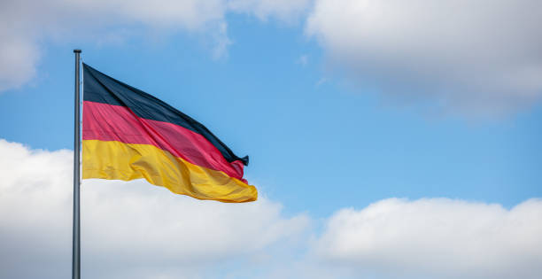 istock German flag waving on flagpole. Cloudy blue sky background, copyspace, banner. 1056600978