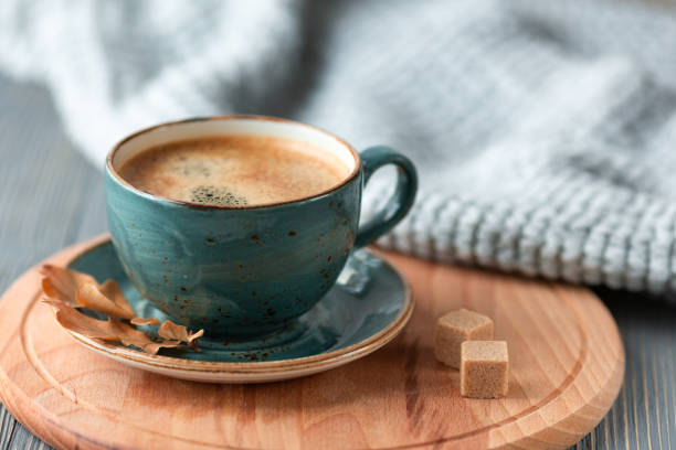 Blue cup whith coffee, knitted sweater, autumn leaves on wooden background. stock photo