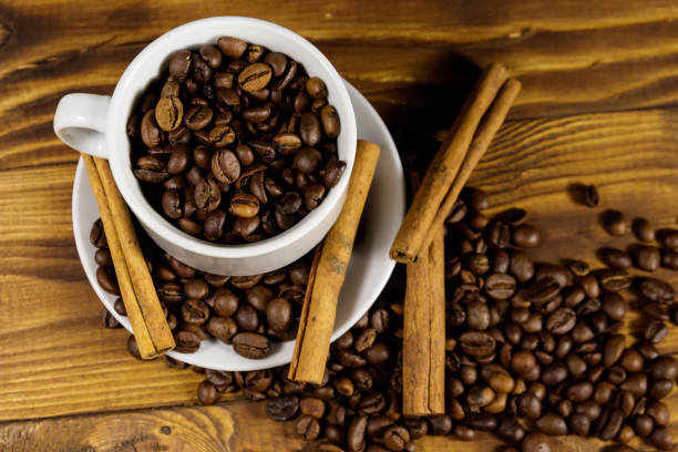istock Coffee beans in white cup and cinnamon sticks on wooden table. Top view 1056609886
