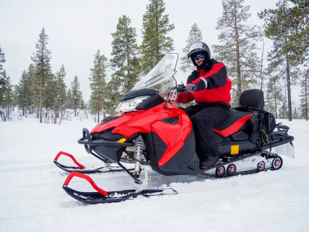 Happy smiling man driving snowmobile in Finnish Lapland