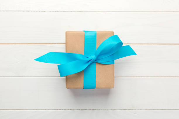 istock Gift box with blue bow over white wooden table with copy space. top view 1056627734