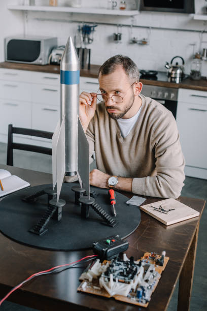istock handsome engineer looking above glasses at rocket model at home 1056632162