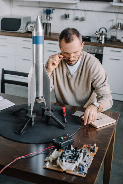 istock handsome engineer modeling rocket and looking above glasses at table at home 1056632168