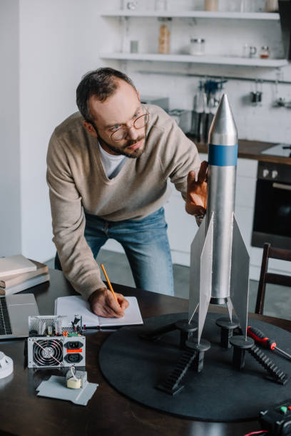 handsome engineer modeling and measuring rocket at home handsome engineer modeling and measuring rocket at home model rocket stock pictures, royalty-free photos & images