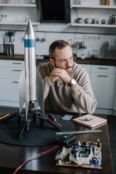 istock pensive engineer sitting at table with rocket model at home and looking away 1056632208