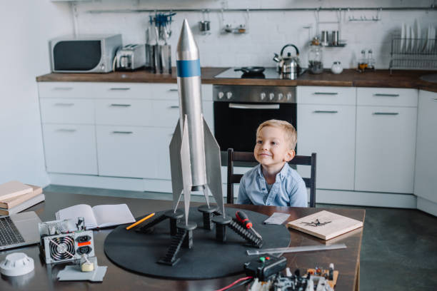 istock cheerful adorable boy sitting at table with rocket model in kitchen on weekend 1056632212