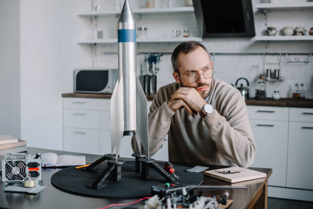 istock thoughtful engineer sitting at table with rocket model at home and looking away 1056632220