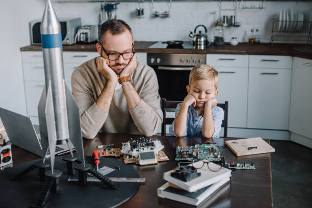 istock pensive father and son looking at circuit board on table at home 1056632416