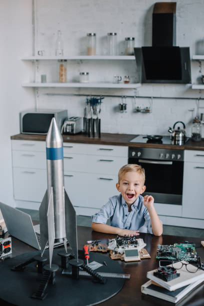 istock happy adorable boy sitting at table with rocket model in kitchen and looking at camera 1056632430