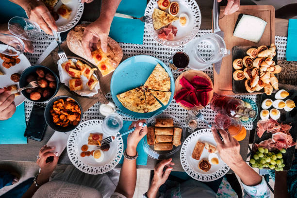 acima vista aérea de um grupo de amigos se divertindo, comendo juntos no almoço ou jantar com uma mesa cheia de coloridos e diferente alimentos e tecnologia celular. mistura de mãos de pessoas caucasianas levando algumas coisas para comer juntos - foodie - fotografias e filmes do acervo