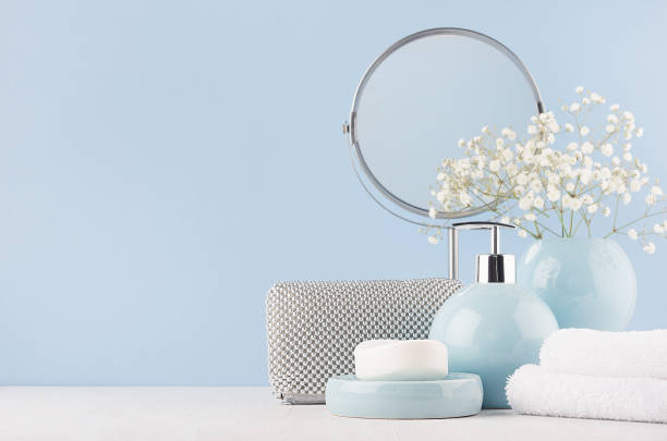 サークル ミラー、銀 cosmrtic バッグ、白い花、タオル、石鹸、白の木のテーブルで滑らかな陶製の花瓶 - 柔らかいライトブルー色の女性のための浴室の装飾。