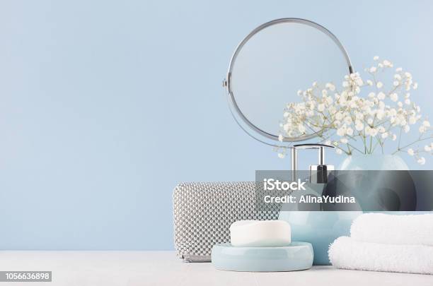 Bathroom Decor For Female In Light Soft Blue Color Circle Mirror Silver Cosmrtic Bag White Flowers Towel Soap And Ceramic Smooth Vase On White Wood Table Stock Photo - Download Image Now