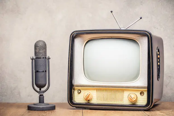 Photo of Retro old TV set and aged microphone front concrete wall background. Broadcasting concept. Vintage style filtered photo