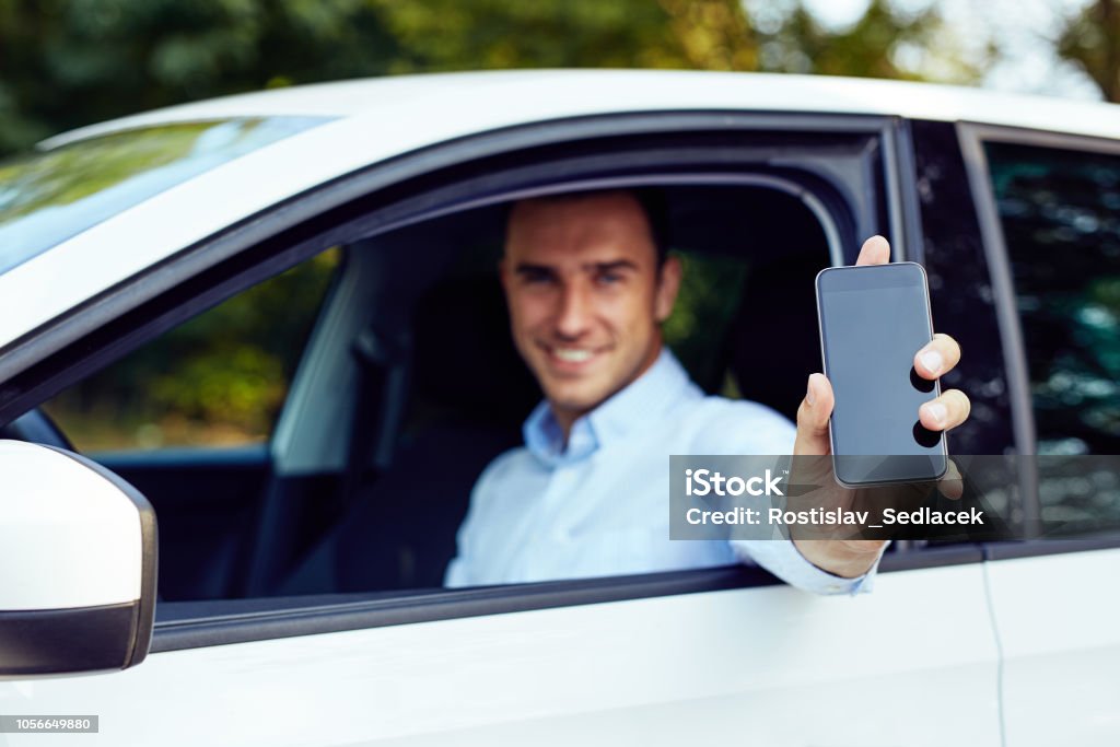 Un hombre sentado en un coche muestra un teléfono móvil - Foto de stock de Conducir libre de derechos