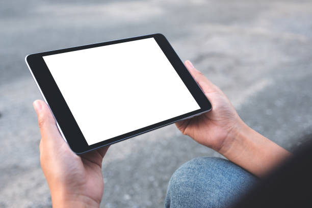 istock Mockup image of a woman holding black tablet pc with blank white screen while sitting on the street background 1056655392