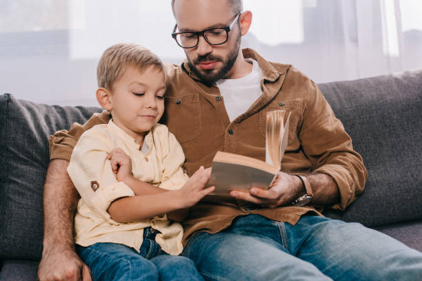 istock father and son sitting on couch and reading book together 1056656276