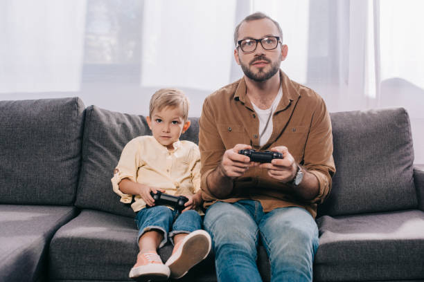 istock father and little little son sitting on couch and playing with joysticks 1056656320