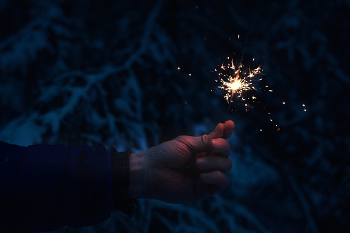 Sparkler in hands on the background of the night winter forest.