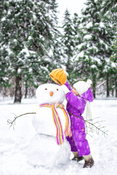 bambino scolpisce un pupazzo di neve in un parco innevato. attività all'aria aperta invernali - snowman snow winter fun foto e immagini stock