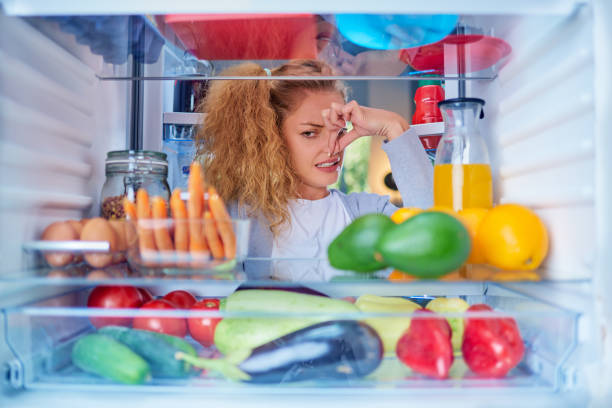 Woman standing in front of opened fridge and holding up to her nose. Woman standing in front of opened fridge and holding up to her nose because of bad smell. Picture taken from the inside of fridge full of groceries. unpleasant smell stock pictures, royalty-free photos & images