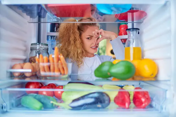 Photo of Woman standing in front of opened fridge and holding up to her nose.