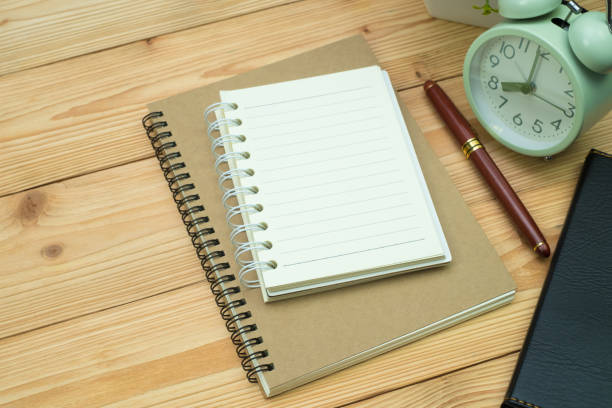 istock Office supplies or office work essential tools items on wooden desk in workplace, pen with notebook and alarm clock. 1056667832